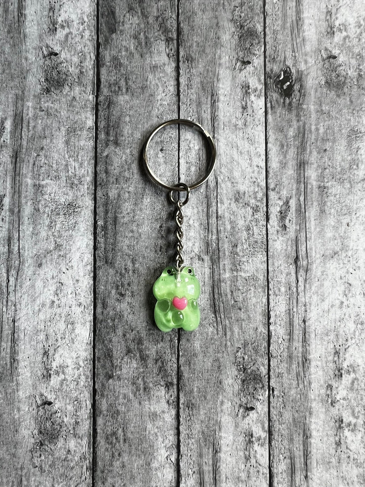 The Frog is made out of a clear resin with a green background. The frog is holding a cute dark pink heart.