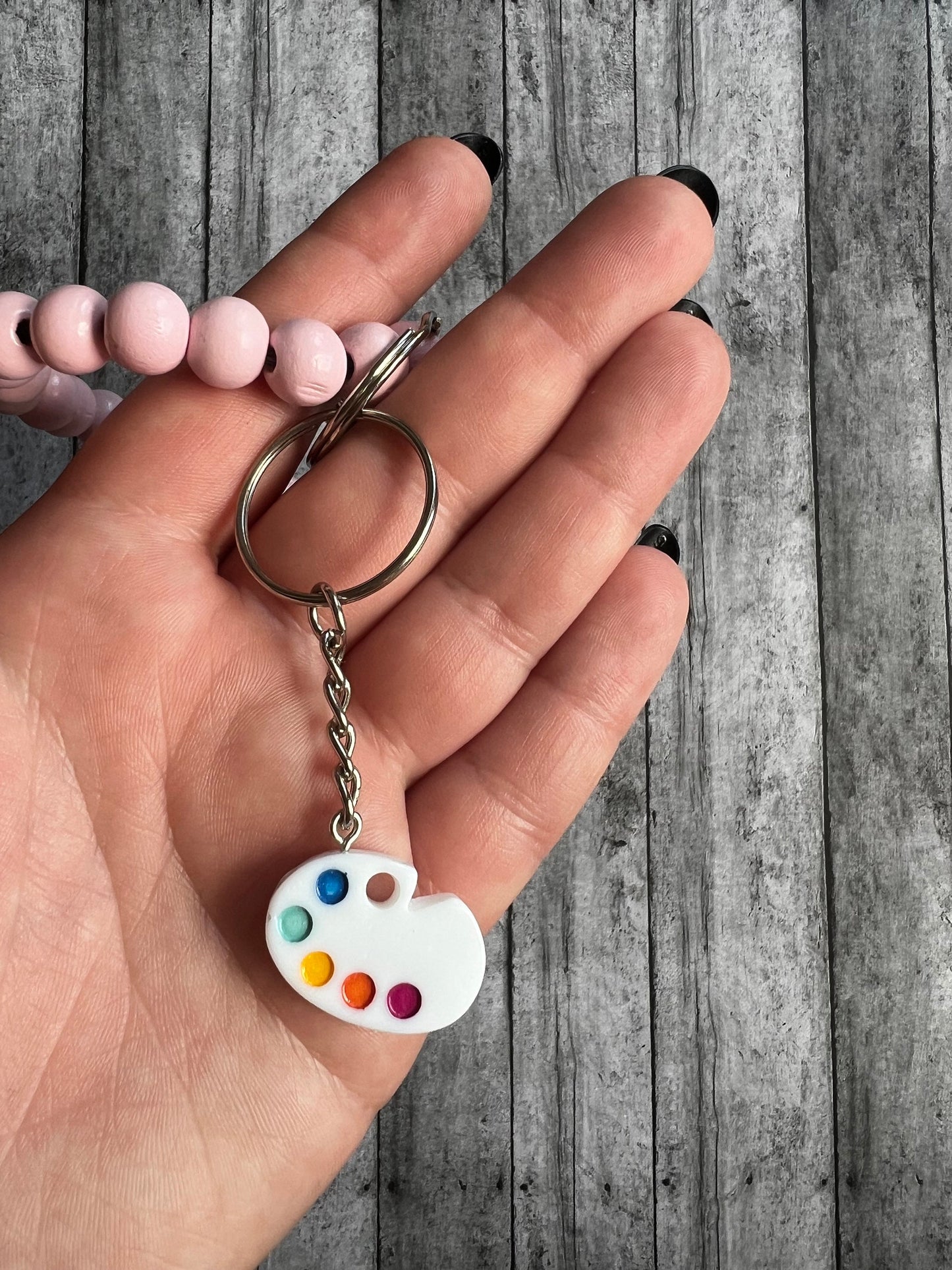 Closer view of the painters palette keychain. the keychain that hooks onto your item of choice is silver.